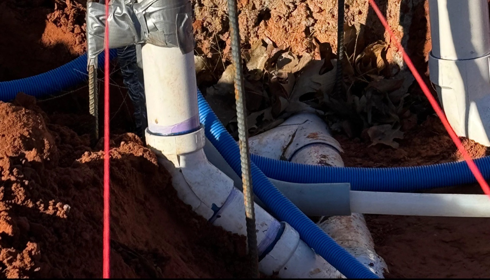 New PVC drain lines and conduit laid in an open trench before a slab pour